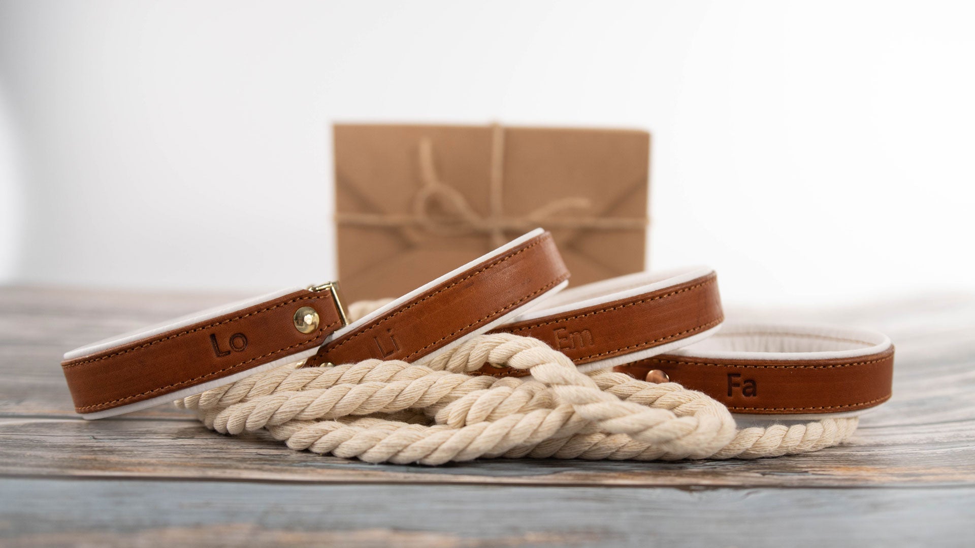 handgefertigte Fettlederhalsbänder liegen auf einem beigen tau, im hintergrund steht eine Geschenkverpackung und alles liegt auf einem holzboden