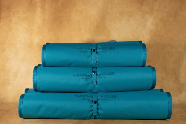 handgefertigtes-hunde-reisebett-von-handmade-4-dogs-gerollt-in-der-Farbe-türkis-mit-einer-kuscheligen-liegefläche-in-der-Farbe-Blutorange-einem-weichen-und-armen-orangeton