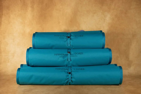 handgefertigtes-hunde-reisebett-von-handmade-4-dogs-gerollt-in-der-Farbe-türkis-mit-einer-kuscheligen-liegefläche-in-der-Farbe-Blutorange-einem-weichen-und-armen-orangeton