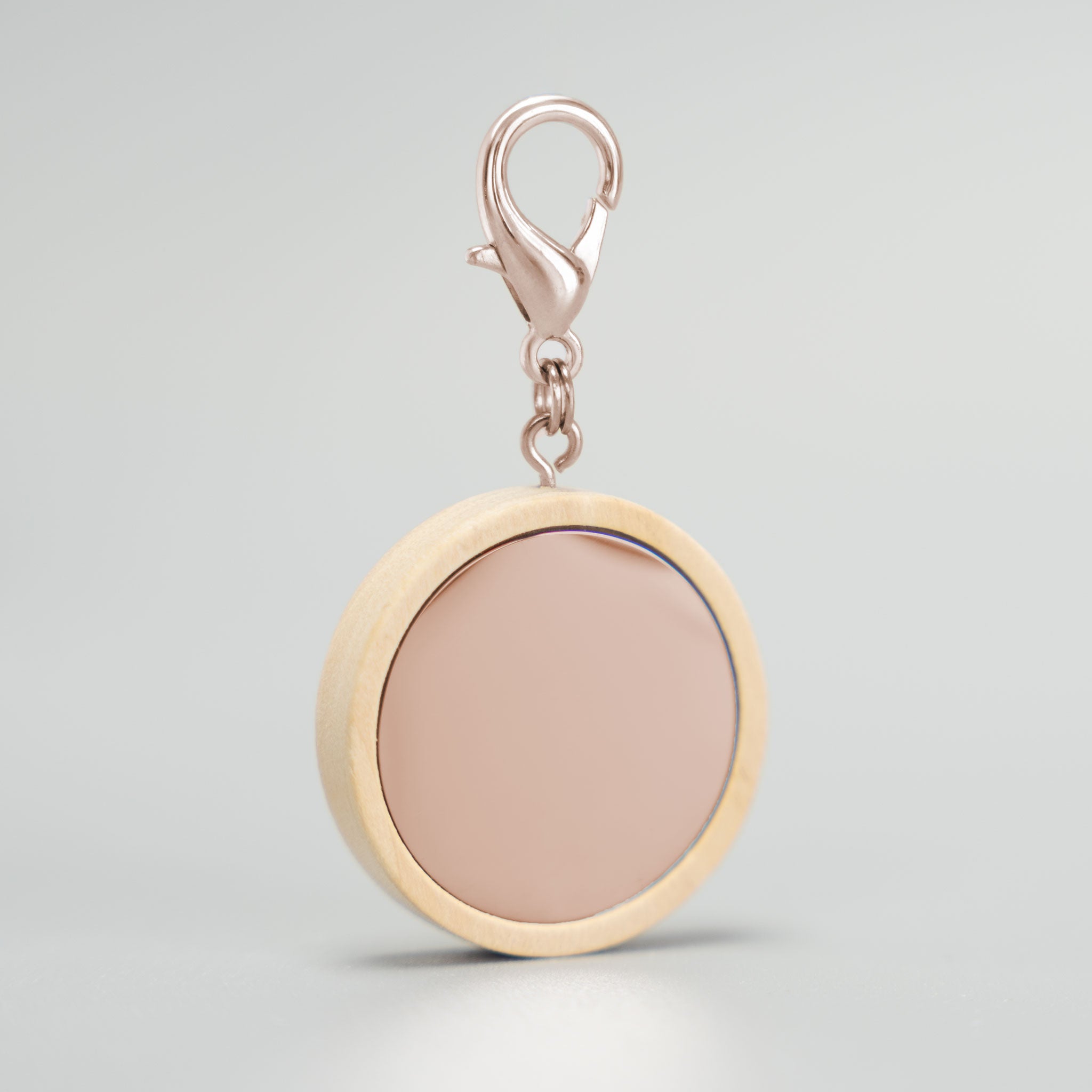 Runde, unbeschriftete Hundemarke mit hellem Holzrahmen, glänzendem Roségold-Inlay und passendem roségoldenem Karabinerverschluss vor einem grauen Hintergrund. Ideal für individuelle Gravuren.