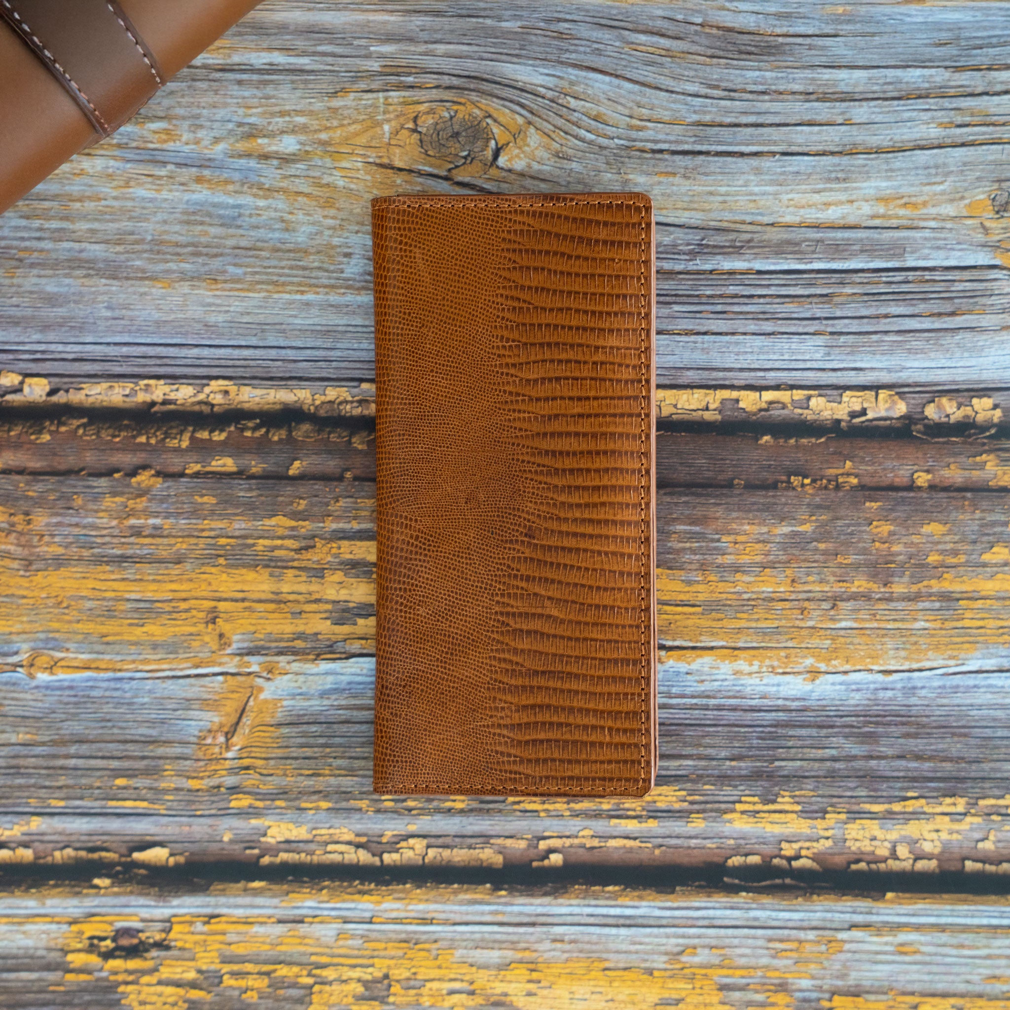 Handgefertigtes Long Wallet aus cognacfarbenem Kalbsleder mit edler Echsenprägung auf einem rustikalen Holzhintergrund – Draufsicht geschlossen.
