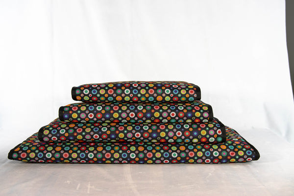 handgefertigtes-hunde-reisebett-von-handmade-4-dogs-im-gerollten-modell-das-Hundereisebett-ist-mit-vielen-bunten-punkten-am-aussenmaterial-überzogen-eingefaßt-ist-es-schwarz-und-innen-bildet-ein-122-unzen-denim-die-4cm-dicke-liegefläche