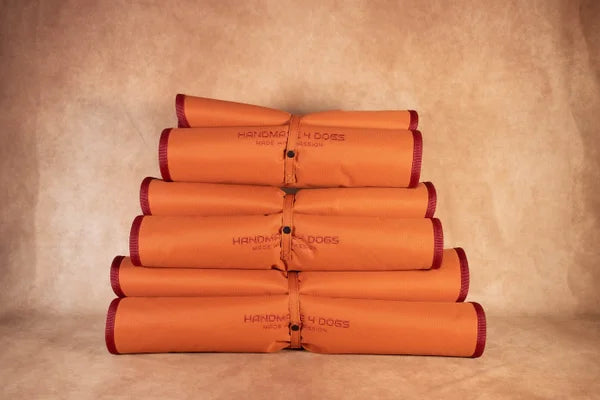 handgefertigtes-Hundereisebett-in-der-gerollten-Version-in-orange-außen-mit-einer-weinroten-einfassung-und-einer-dicken-liegefläche-in-einem-weinrot-gefertigt-aus-deinem-dicken-kuschelmaterial-alles-ist-waschbar