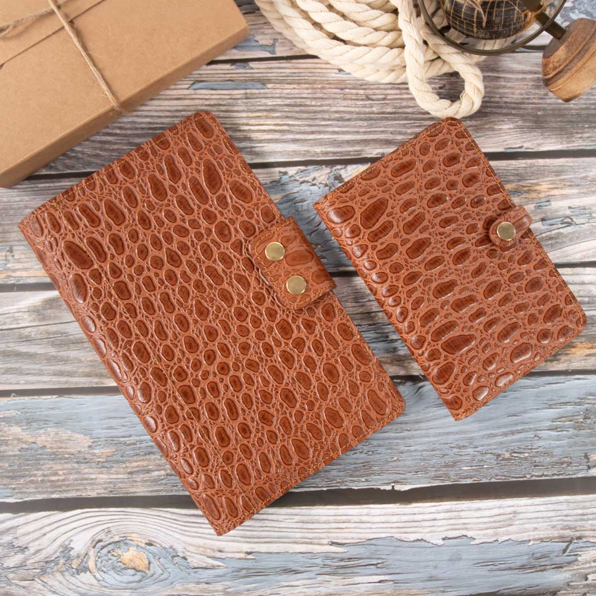 Gegenüberstellung des cognacfarbenen Kroko-Leder Travel Wallets und der passenden EU-Heimtierausweishülle, die den Größenunterschied der beiden handgefertigten Etuis verdeutlicht.