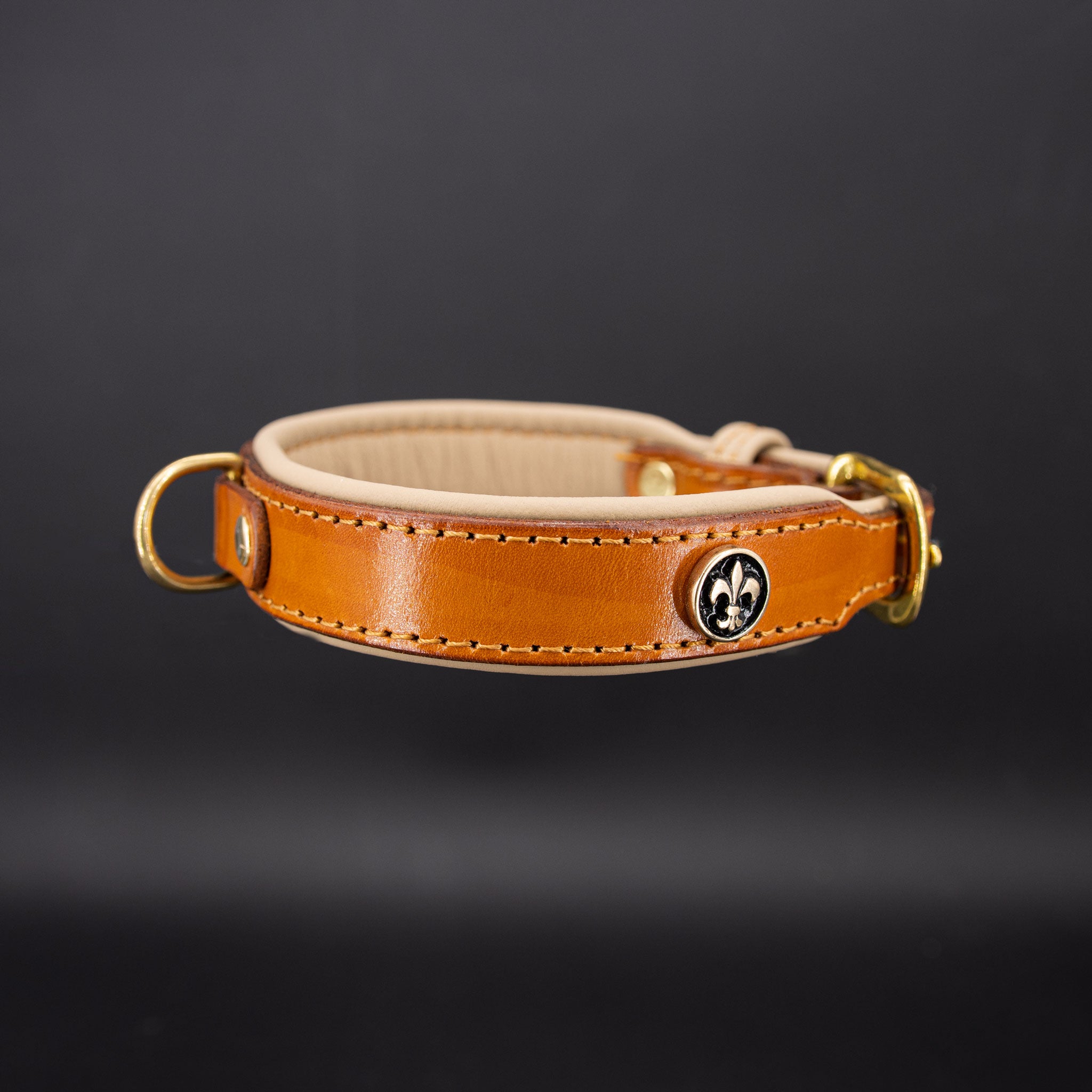 Detailansicht des 14 Karat vergoldeten Fleur de Lys Beschlags auf cognacfarbenem Leder