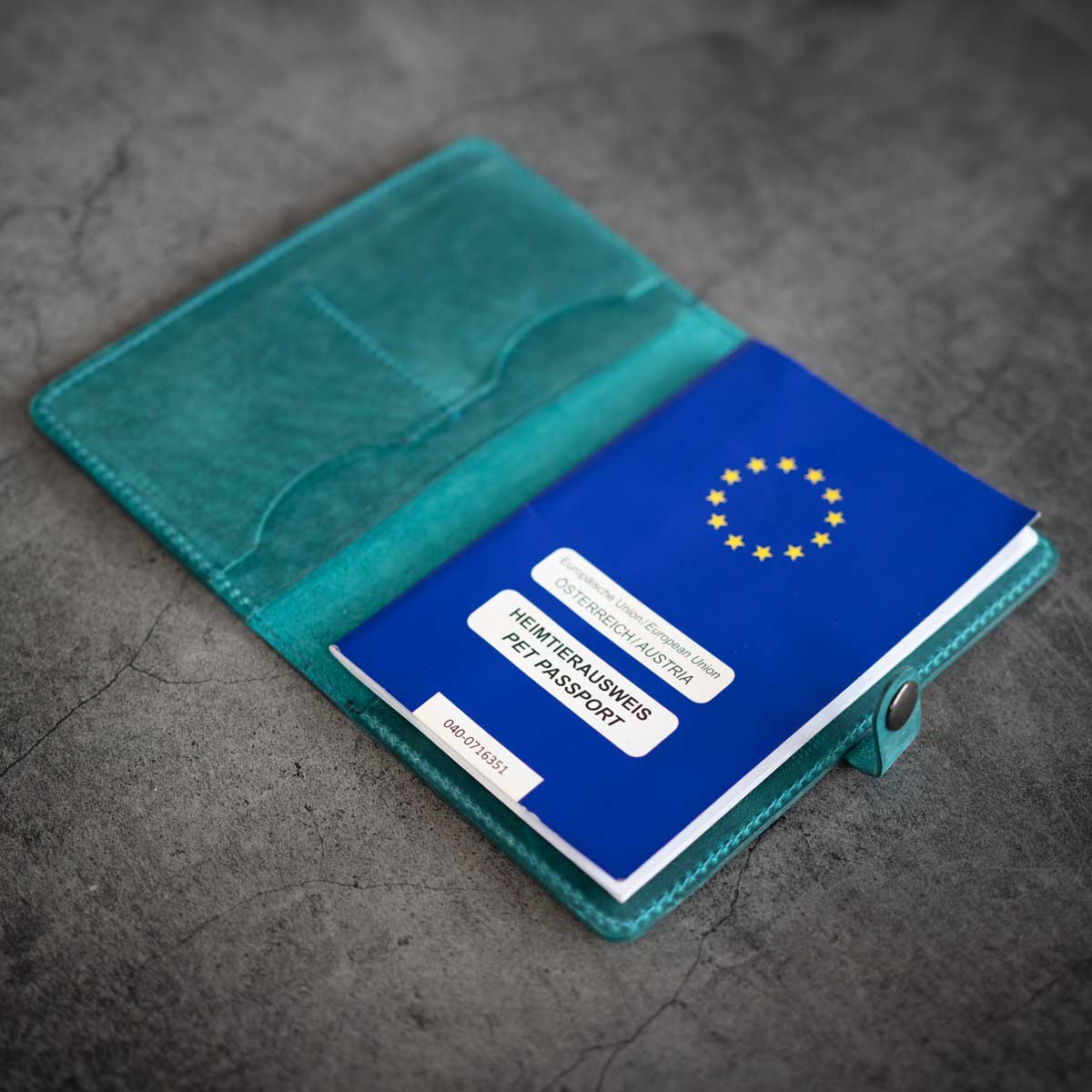 Geöffnete türkisfarbene Leder-Impfpasshülle, befüllt mit einem blauen EU-Heimtierausweis und einer Verschlusslasche.