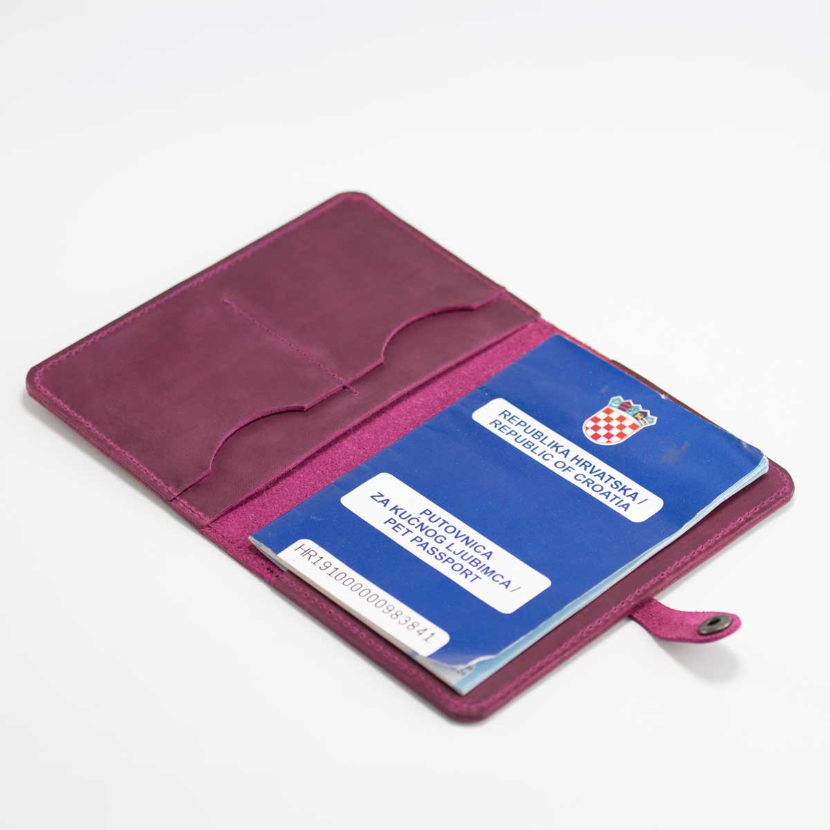 Geöffnete Impfpasshülle aus Leder in Wild Berry, befüllt mit einem blauen EU-Heimtierausweis und sichtbaren Kartenfächern.