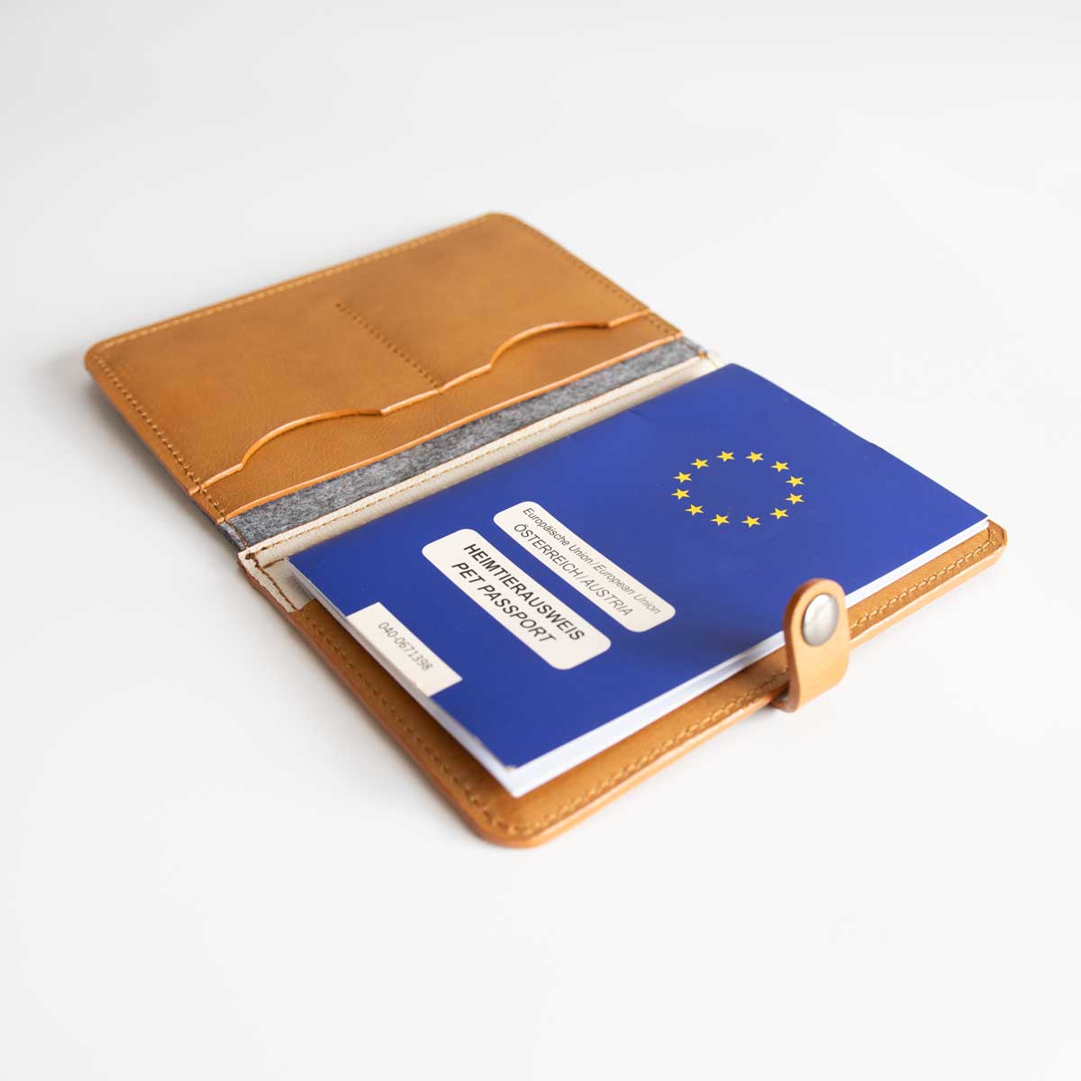 Geöffnete Impfpasshülle aus Leder und Filz, befüllt mit einem blauen EU-Heimtierausweis und Tierarztunterlagen.