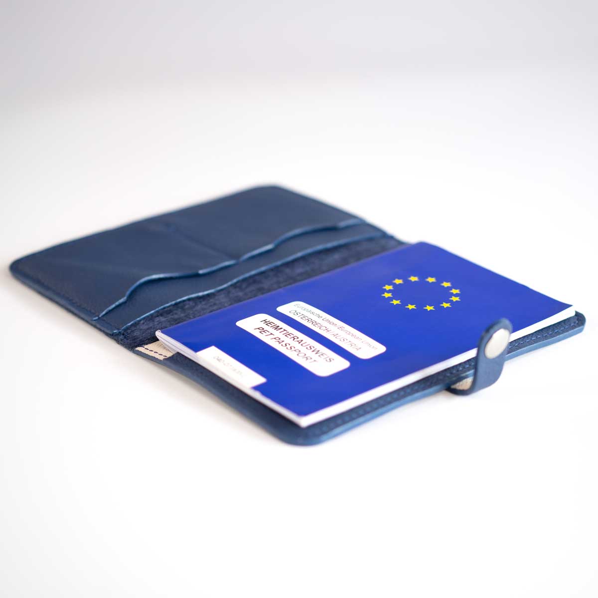 Geöffnete Heimtierausweishülle in Navy-Blau, sicher befüllt mit einem blauen EU-Heimtierausweis und Dokumenten.