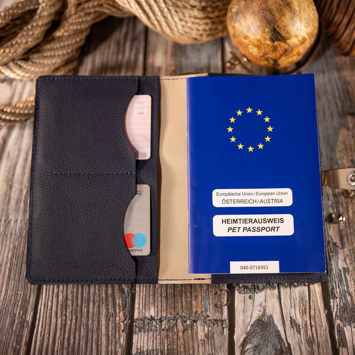 Geöffnete dunkelblaue Leder-Impfpasshülle mit elegantem taupefarbenem Innenfutter und einem eingesteckten blauen EU-Heimtierausweis.