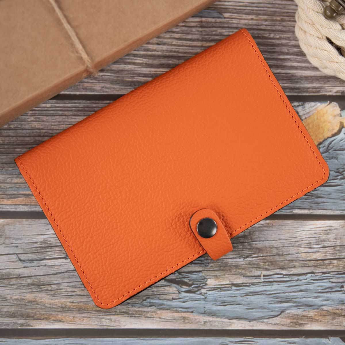 Vorderseite der geschlossenen Heimtierausweishülle aus orangem Leder mit schwarzen Kontrastkanten und einer Lasche mit gunfarbenem Druckknopf.