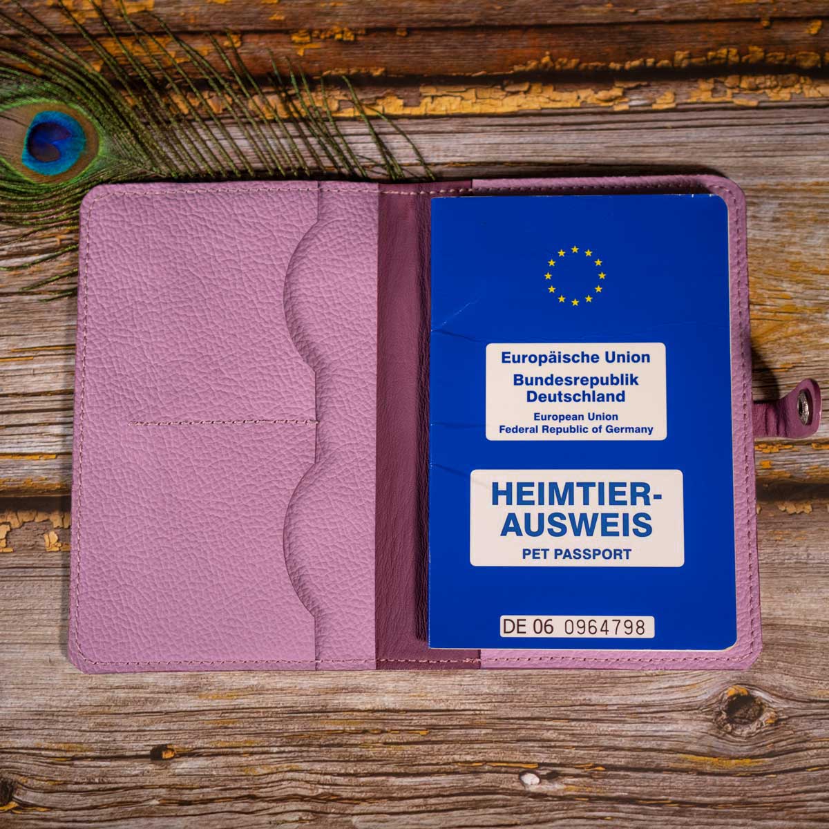 Geöffnete Heimtierausweishülle aus orchideefarbenem Leder, befüllt mit einem blauen EU-Heimtierausweis auf der rechten Seite.