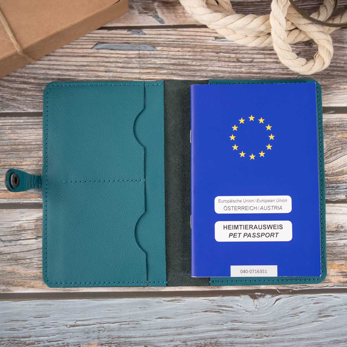 Geöffnete Leder-Impfpasshülle in Petrol, befüllt mit einem blauen EU-Heimtierausweis auf der rechten Seite und Sicht auf die präzisen Handnähte.