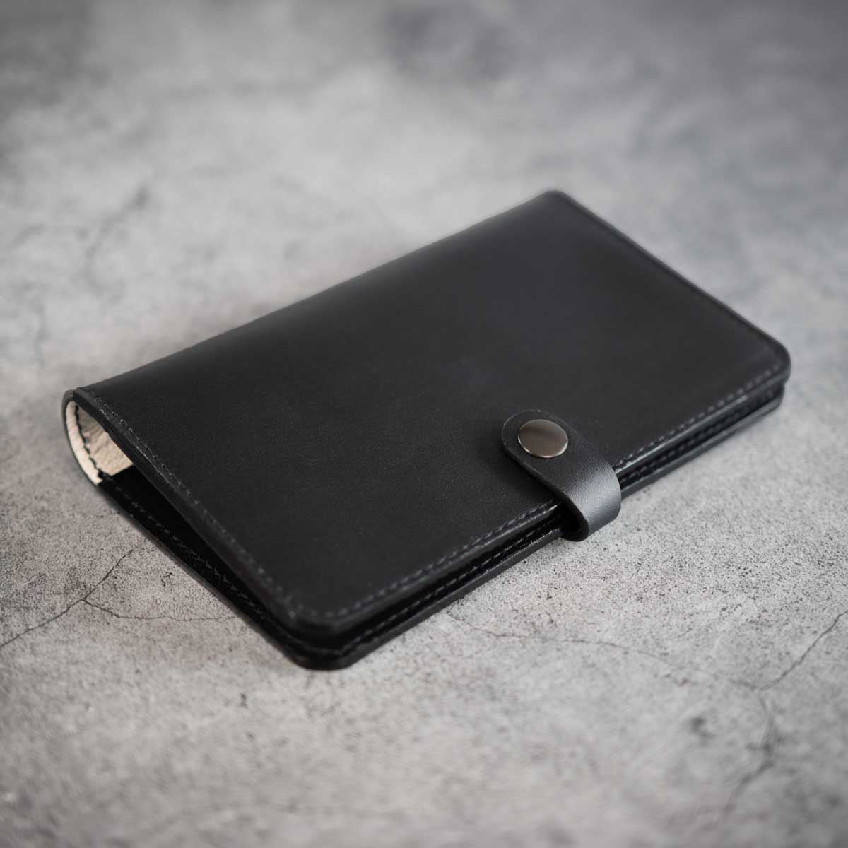 Vorderseite der geschlossenen Premium-Heimtierausweishülle aus schwerem schwarzem italienischem Leder mit einer Druckknopf-Lasche in Gunmetal.