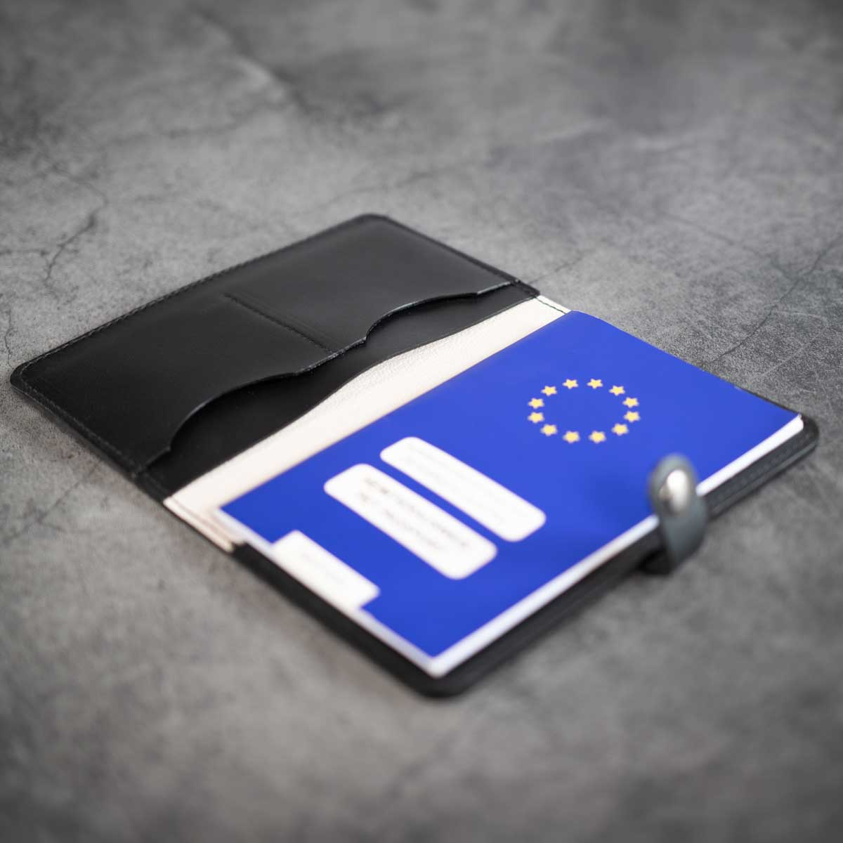 Geöffnete schwarze Impfpasshülle aus Leder mit edlem Off-White Kalbslederfutter und einem eingesteckten blauen EU-Heimtierausweis