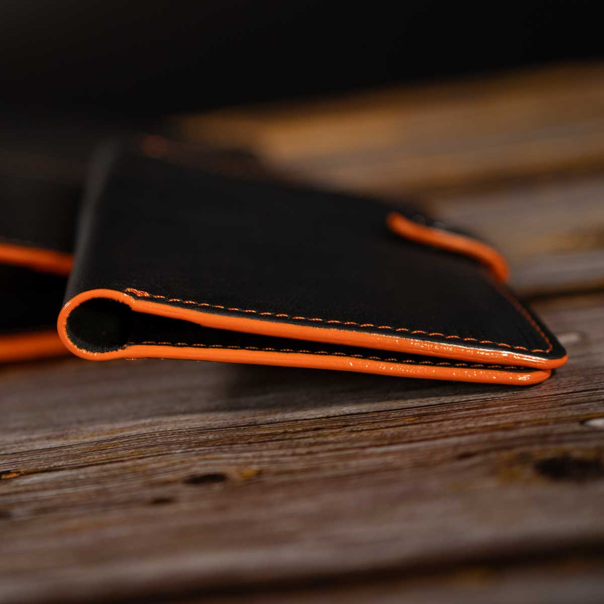 Detailansicht der präzisen orangefarbenen Kontrastnähte auf dem schweren, feinnarbigen schwarzen italienischen Taschenleder.