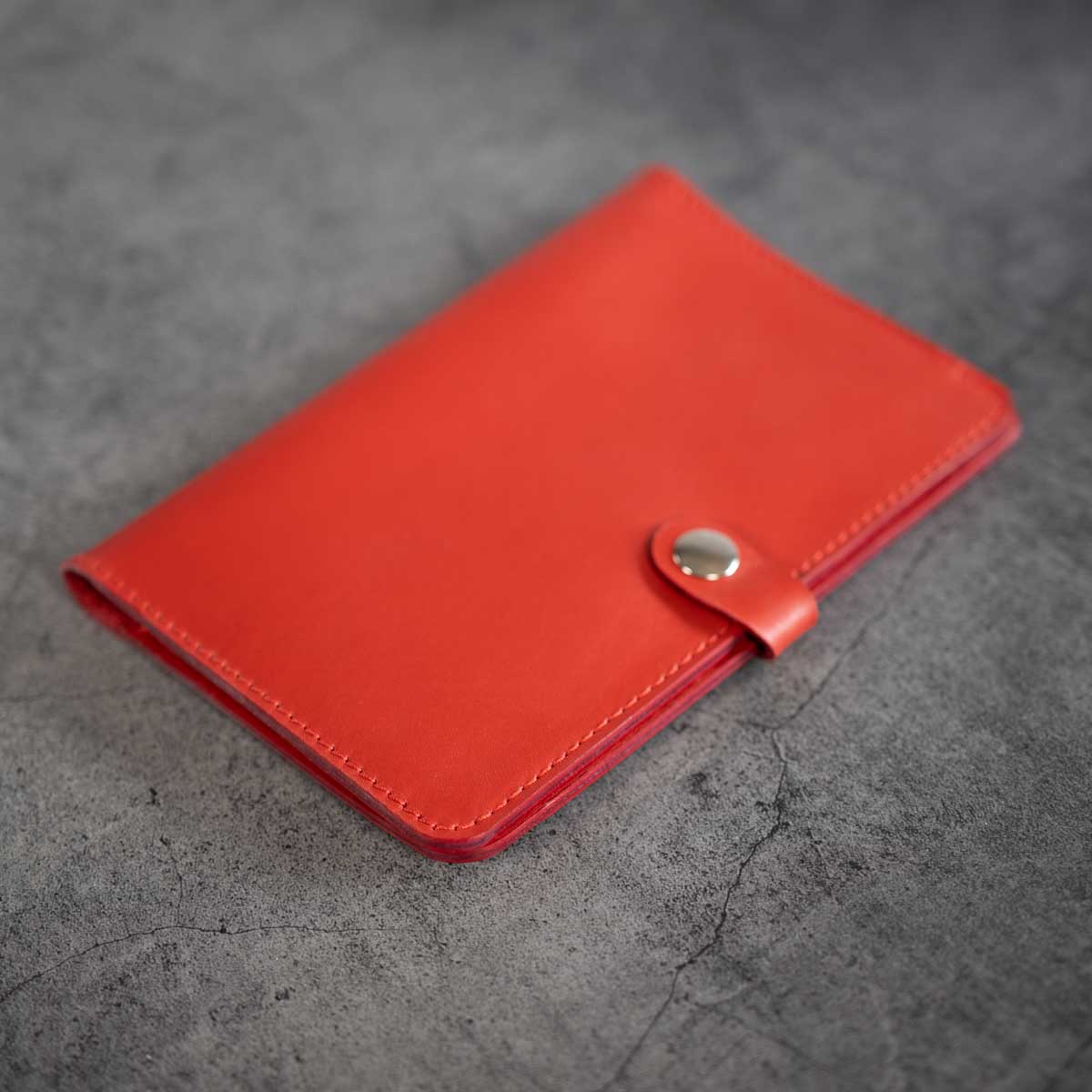 Vorderseite der geschlossenen Heimtierausweishülle aus signalrotem italienischem Leder mit eleganter Verschlusslasche und silbernem Druckknopf.