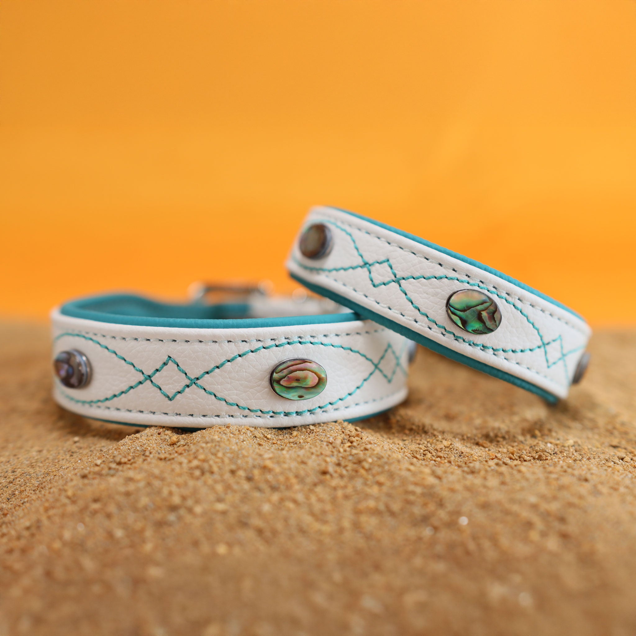 Weißes Lederhalsband mit türkiser Polsterung und Abalone Muscheln auf Sand