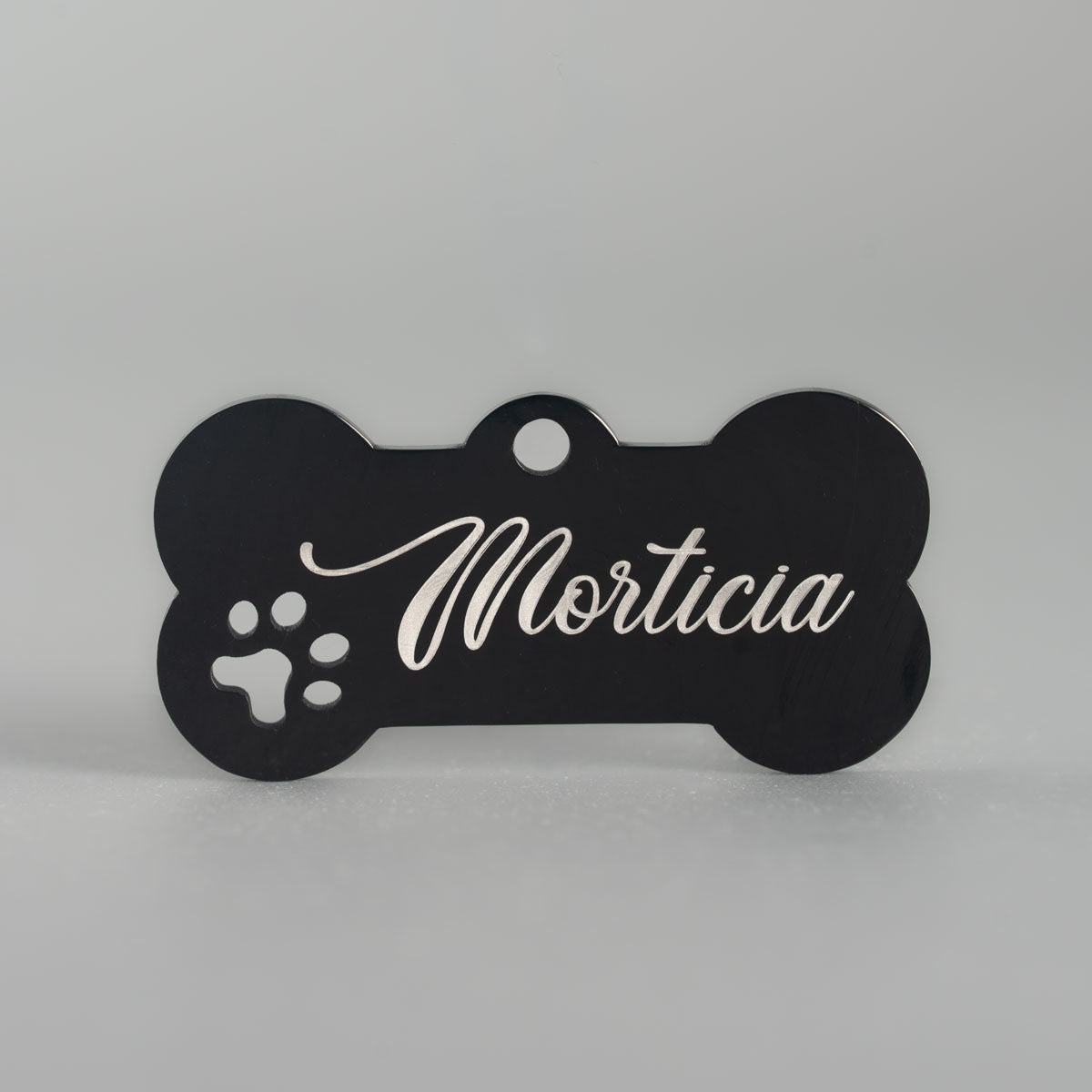 Schwarze Edelstahl-Hundemarke in Knochenform mit Pfötchen-Cut-out und heller Namensgravur Morticia.