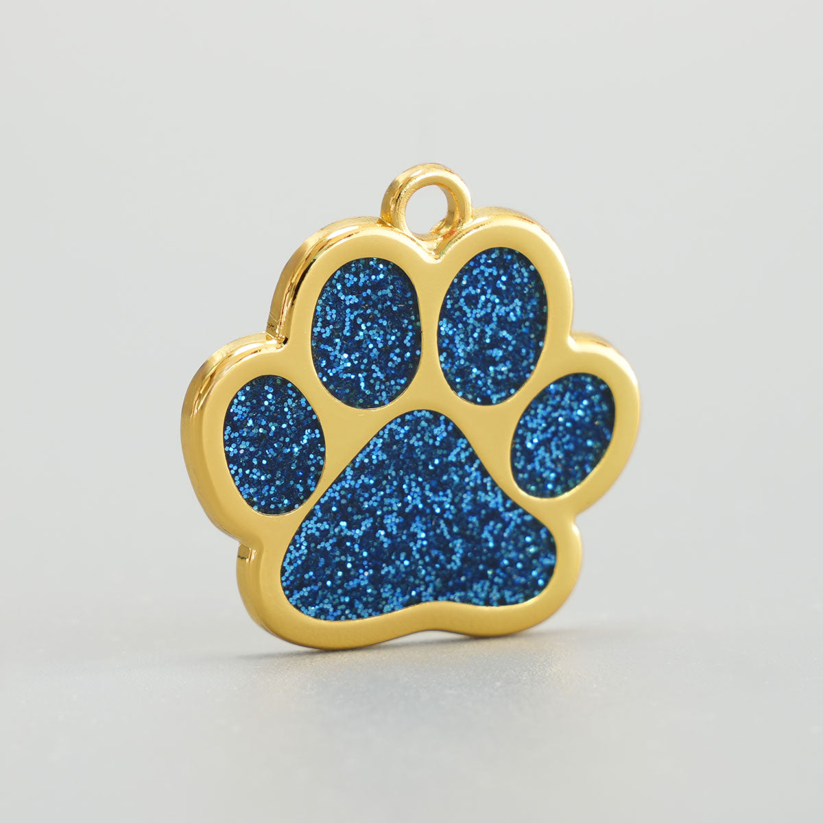 Nahaufnahme einer goldenen Hundemarke in Pfotenform mit blauem Glitzer-Epoxidharz und Aufhängung.