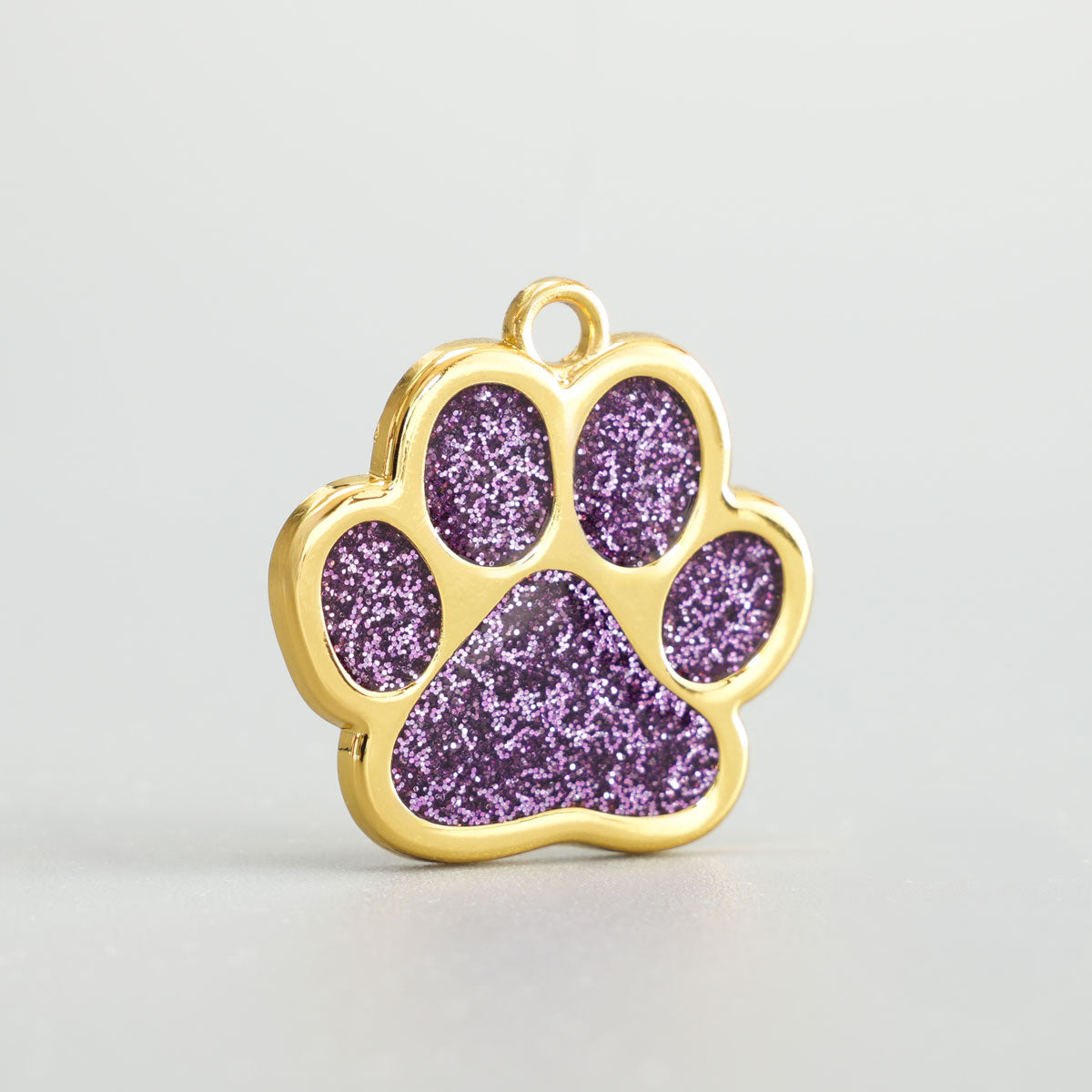 Nahaufnahme einer goldenen Hundemarke in Pfotenform mit flieder Glitzer-Epoxidharz und Aufhängung.