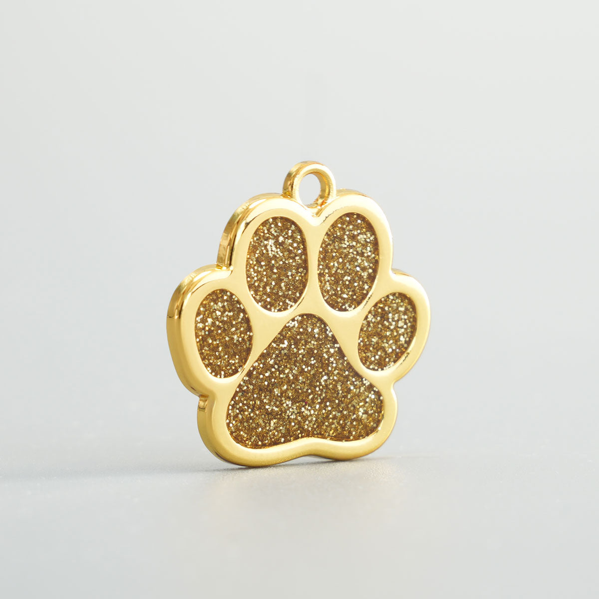 Nahaufnahme einer goldenen Hundemarke in Pfotenform mit goldenem Glitzer-Epoxidharz und Aufhängung.