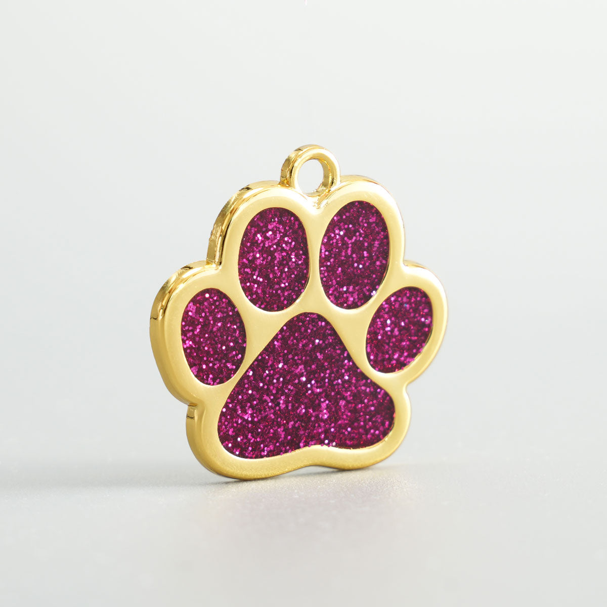 Nahaufnahme einer goldenen Hundemarke in Pfotenform mit magentafarbenem Glitzer-Epoxidharz und Aufhängung.