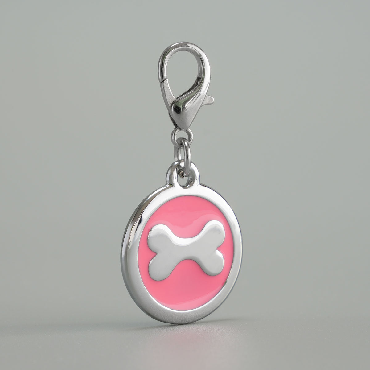 Detailansicht einer pinken, runden Hundemarke aus verchromtem Druckguss mit silbernem Knochen-Inlay und Karabiner