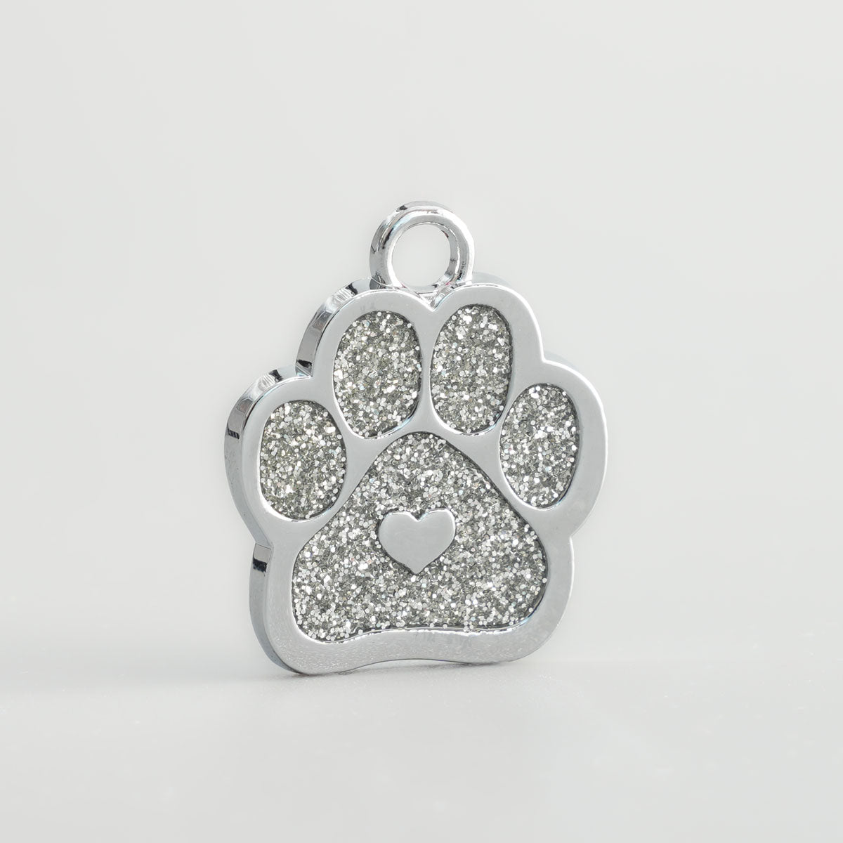 Nahaufnahme einer verchromten Hundemarke in Pfotenform mit silbernem Glitzer-Inlay und silbernem Herz in der Mitte.