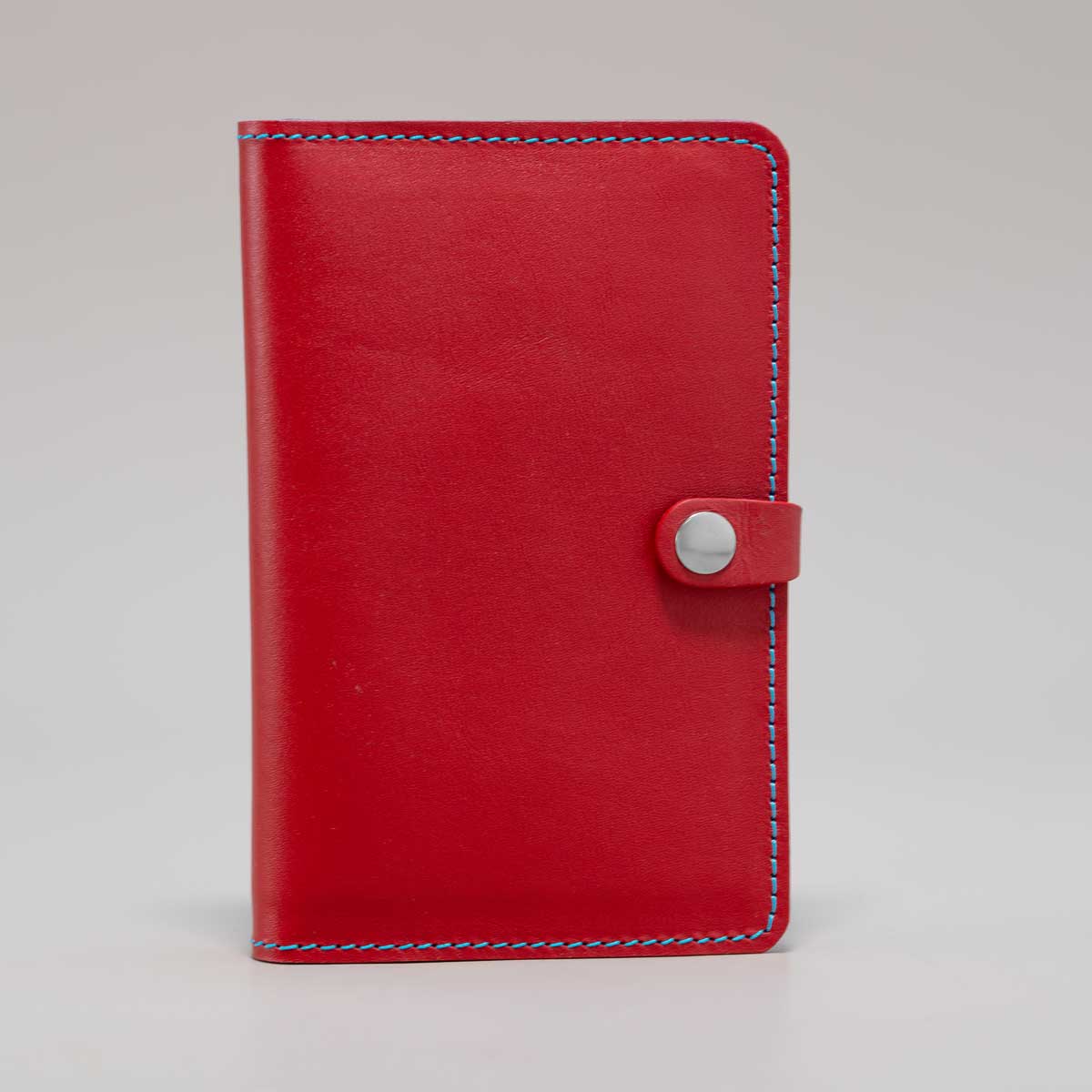 Aufrecht stehende Leder-Impfpasshülle in Signalrot, die das leuchtende Design und die feinen hellblauen Nähte zeigt.