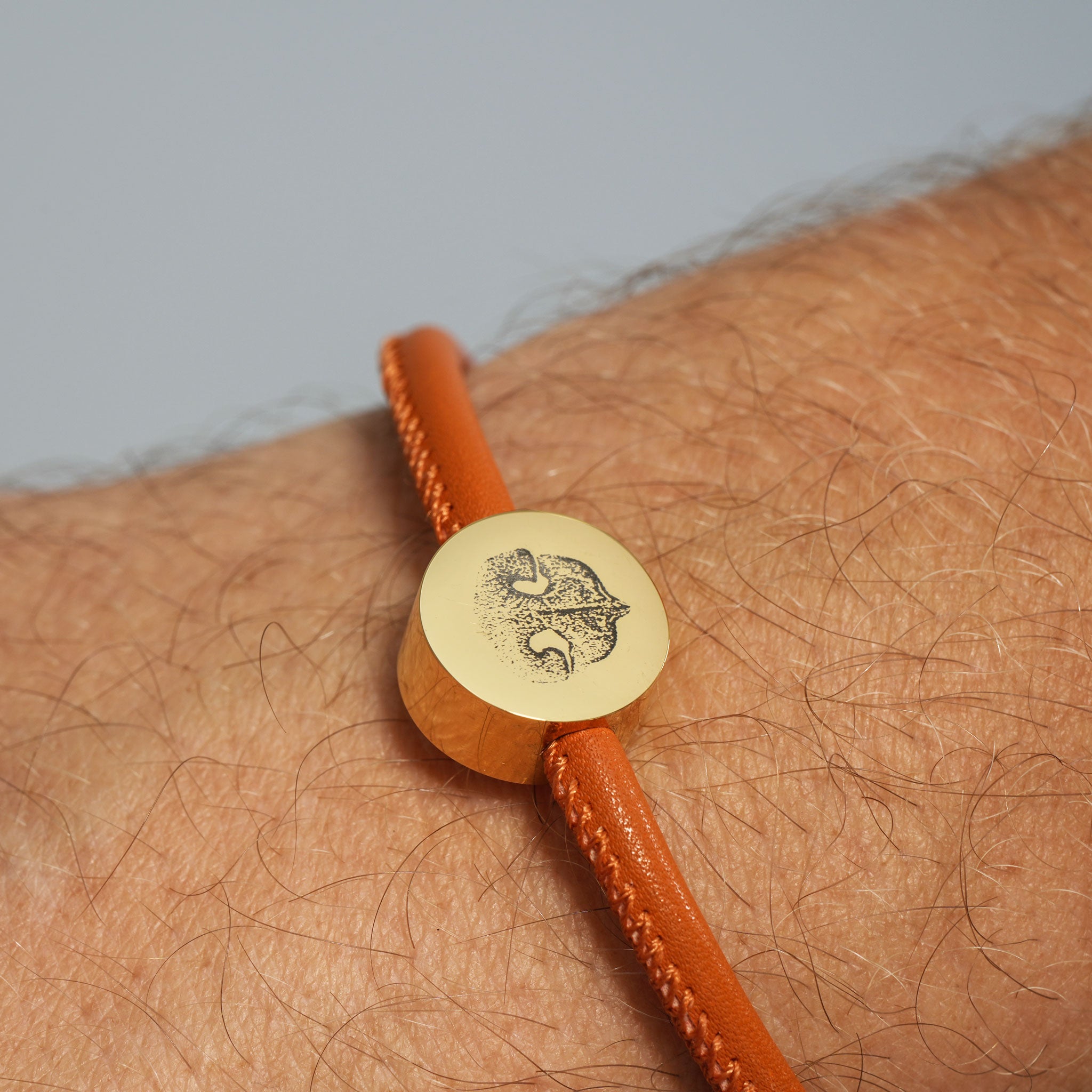 Cognacfarbenes Lederarmband mit goldener Gravur-Perle (Motiv Hundenase), getragen am Handgelenk