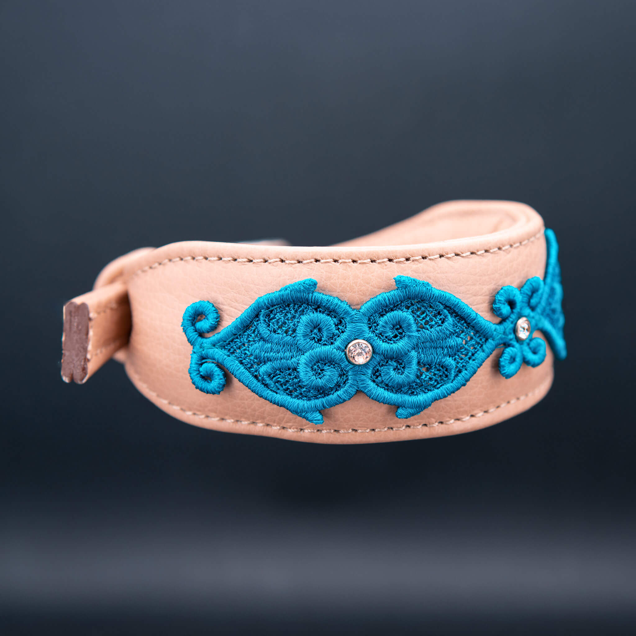 Detailansicht der pfauenblauen Spitze und Stickerei auf sandfarbenem Rindsnappa-Leder