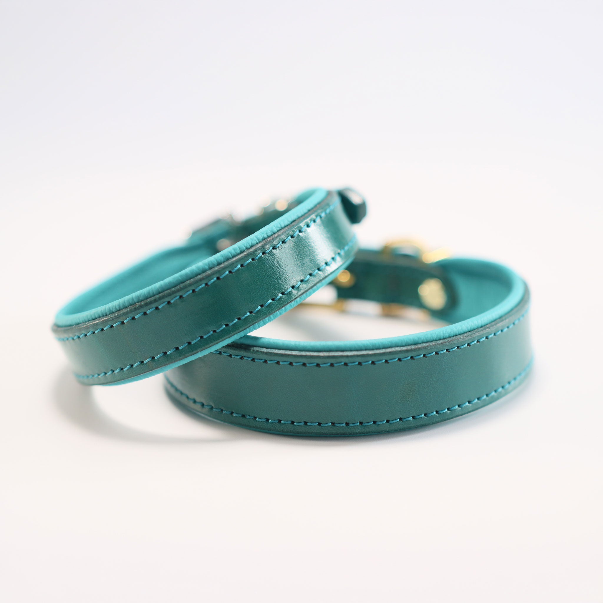 Zwei türkise Lederhalsbänder im Vergleich mit Messing- und Silber-Beschlägen