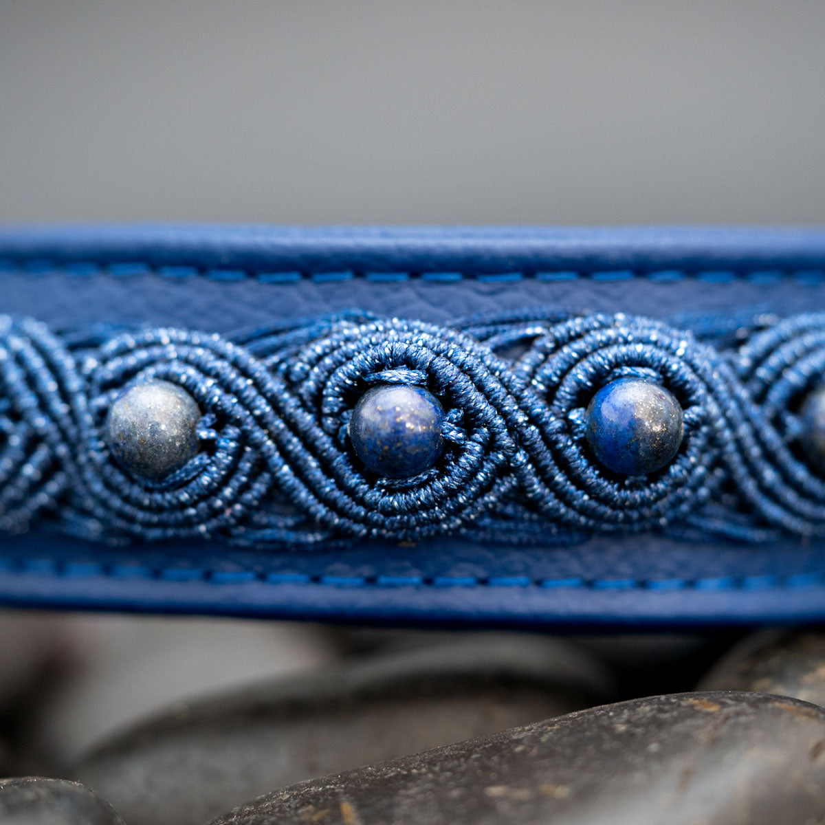 Drei Lapislazuli-Perlen in ovalen blauen Makramee-Motiven; darüber und darunter sind Lederkanten und blaue Nähte sichtbar.