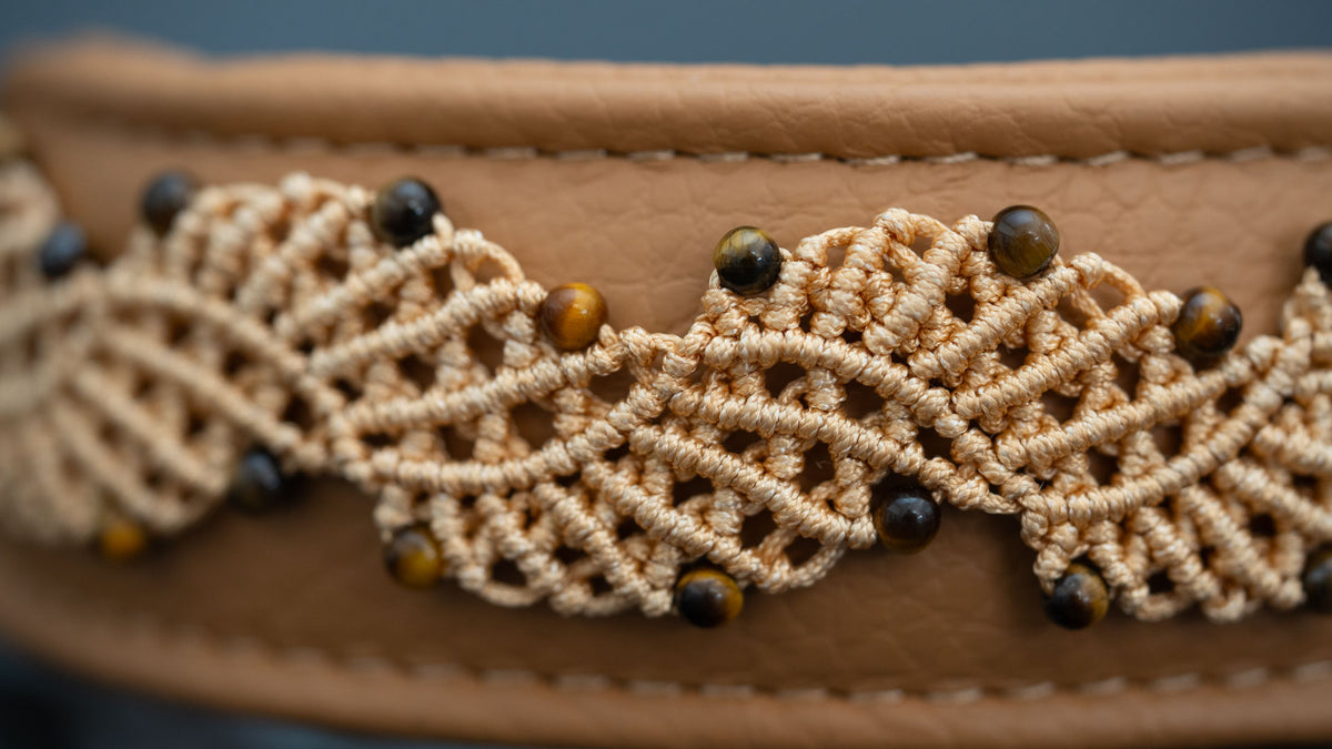 Detail im Querformat: blattähnliche Makramee-Motive in Beige mit goldbraunen Tigerauge-Perlen vor Nappaleder in Cappuccino.