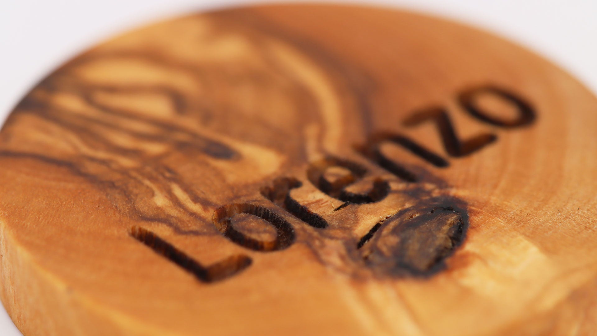 Makroansicht der Olivenholz-Hundemarke nach der Gravur mit dem Namen "Lorenzo"