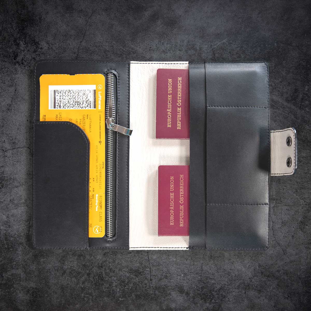 Geöffnetes handgefertigtes Leder Travel Wallet in Schwarz, befüllt mit zwei österreichischen Reisepässen und einer Bordkarte