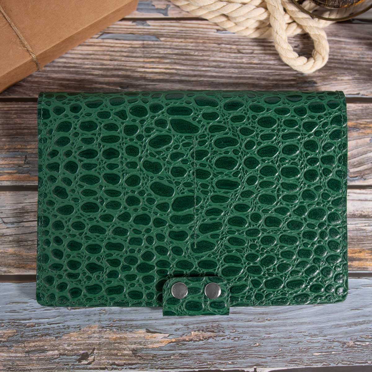 Geschlossenes Travel Wallet für vier Pässe aus grünem Rindsleder mit tiefer Krokodilprägung. Sichtbar ist die markante Verschlusslasche mit zwei edlen, silbernen Druckknöpfen.