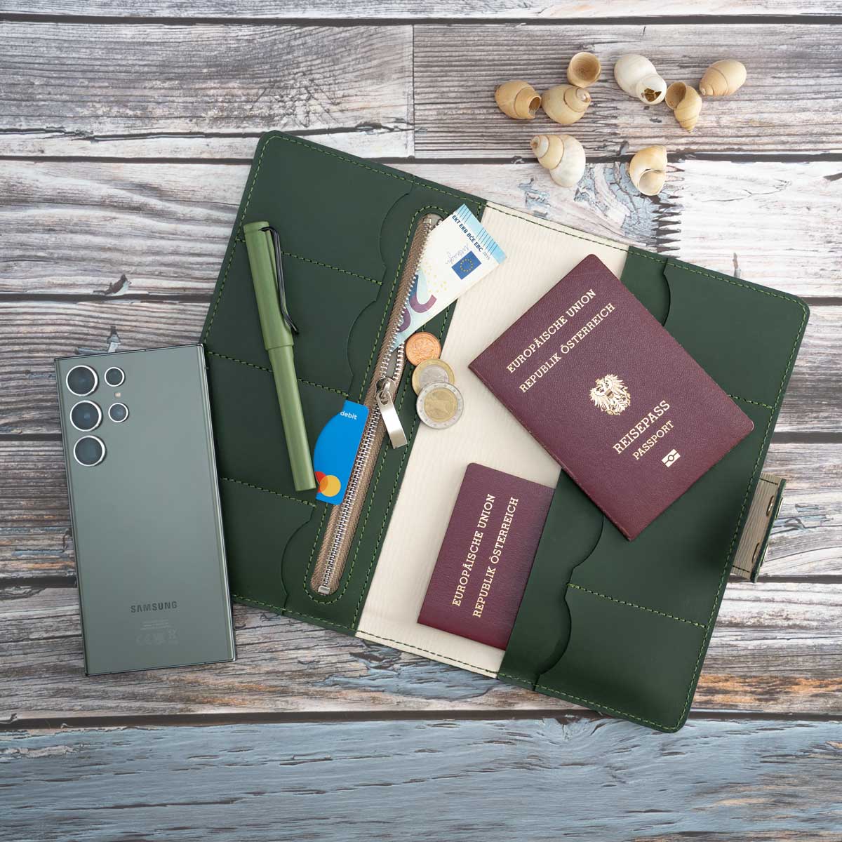Das befüllte Travel Wallet in Dunkelgrün zeigt seine praktische Aufteilung. Neben Reisepässen und Kreditkarten finden in dem großen Reißverschlussfach auch ein EU-Heimtierausweis und ein Smartphone sicheren Platz