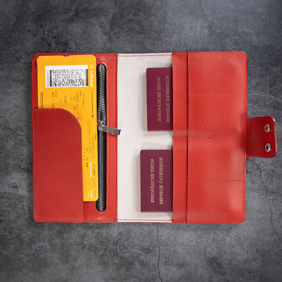 Befülltes rotes Travel Wallet. Die praktische Aufteilung bietet sicheren Platz für zwei Reisepässe, ein langes Flugticket im Einschubfach sowie Kreditkarten