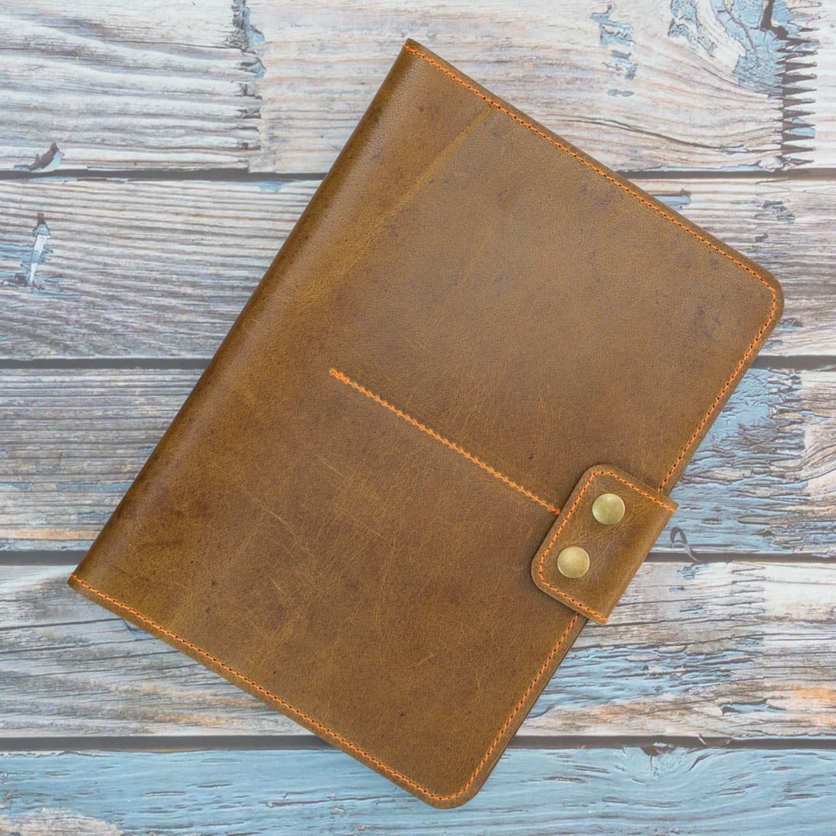 Handgefertigtes Reise-Etui für Pässe. Geschlossen zeigt es das schlammbraune Wasserbüffelleder mit Pull-up-Effekt, orange Kontrastnähte und zwei altmessingfarbene Druckknöpfe