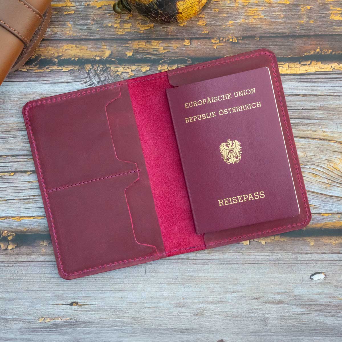 Geöffnete Reisepasshülle aus magentafarbenem Leder mit eingestecktem österreichischen EU-Reisepass auf der rechten Seite.