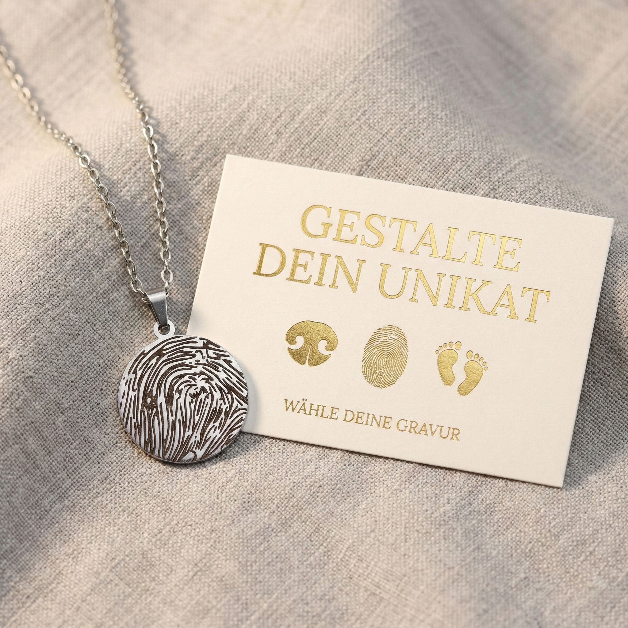 eine boutique-design karte die die Auswahl an Gravurmöglichkeiten für den rechts liegenden Schlüsselanhänger zeigt. auf dem goldenen, runden Schlüsselanhänger ist der Nasenabdruck eines Hundes graviert