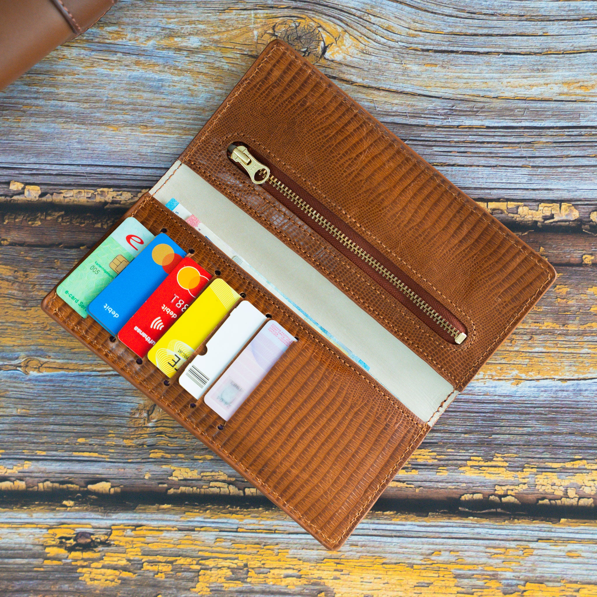 Geöffnetes Leder-Portemonnaie mit Innenfutter aus cremefarbenem Kalbsleder, 6 belegten Kartenfächern und einem Münzfach mit goldfarbenem YKK-Reißverschluss.