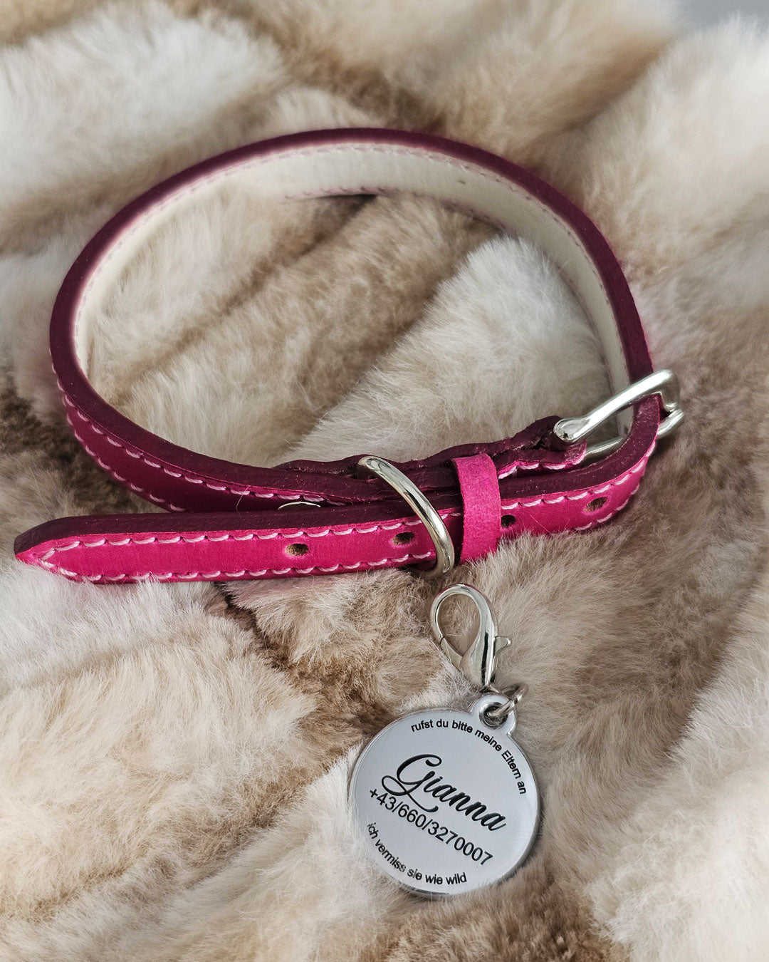 gravierte Edelstahl-Hundemarke liegt auf einem beigen Webpelz neben einem pinken Welpenhalsband
