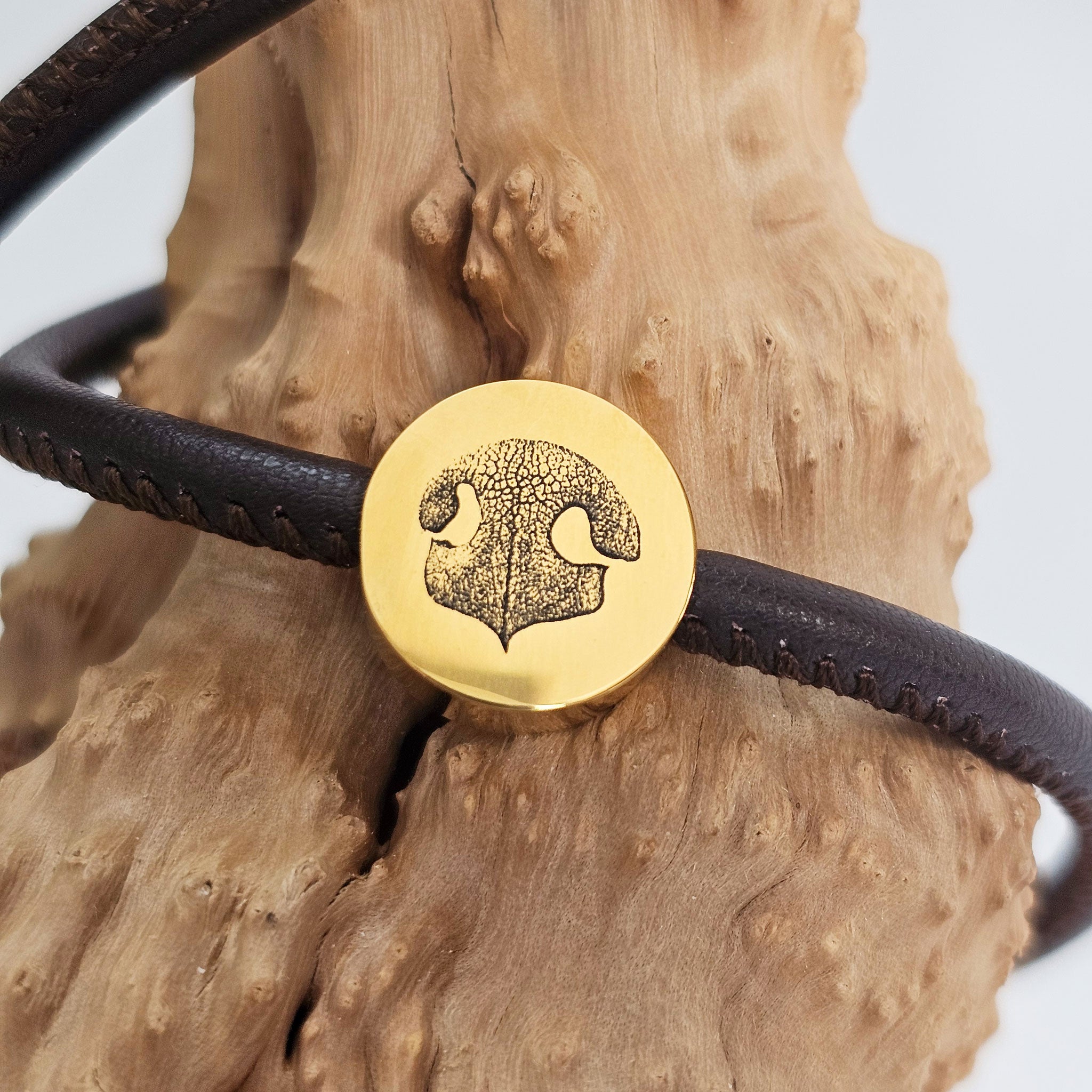 Nahaufnahme einer präzisen Hundenasen-Gravur auf einem goldenen Schmuckelement an einem braunen Lederarmband