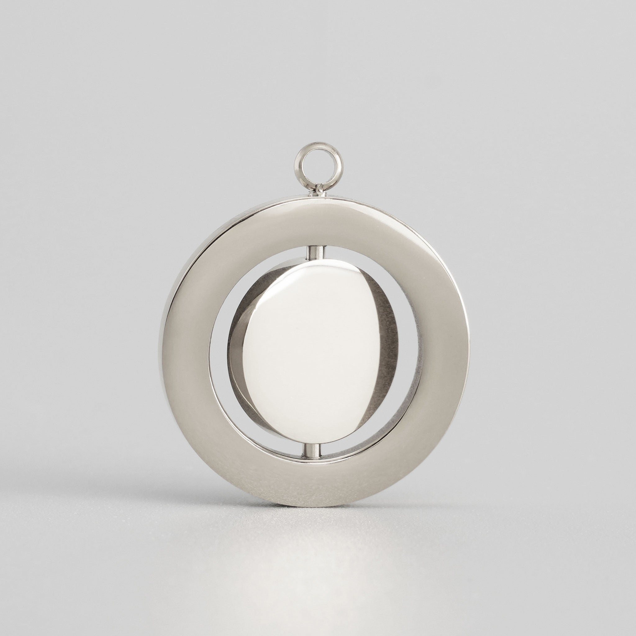 Schlichtes Drehmedaillon aus silberfarbenem Edelstahl vor grauem Hintergrund