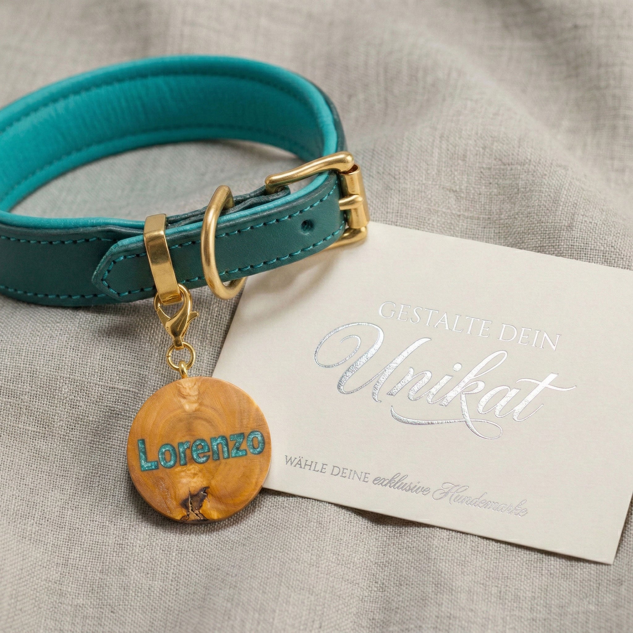 Personalisierte Hundemarke aus Olivenholz mit Epoxy-Inlay an türkisfarbenem Lederhalsband mit Gold-Beschlägen.