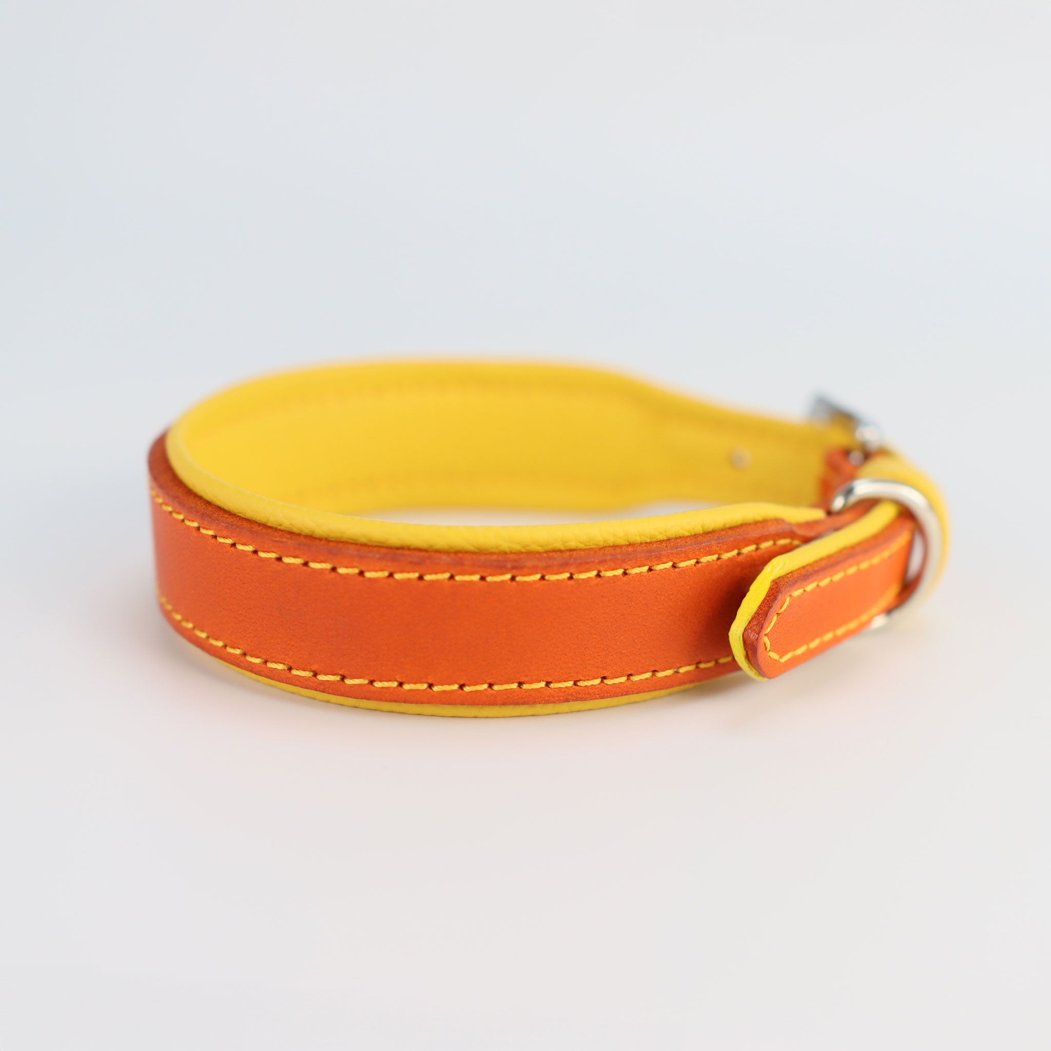 Handgefertigtes Hundehalsband aus orangem Fettleder mit gelber Nappa-Polsterung und gelber Kontrastnaht, flach liegend auf weißem Hintergrund von der seite gesehen