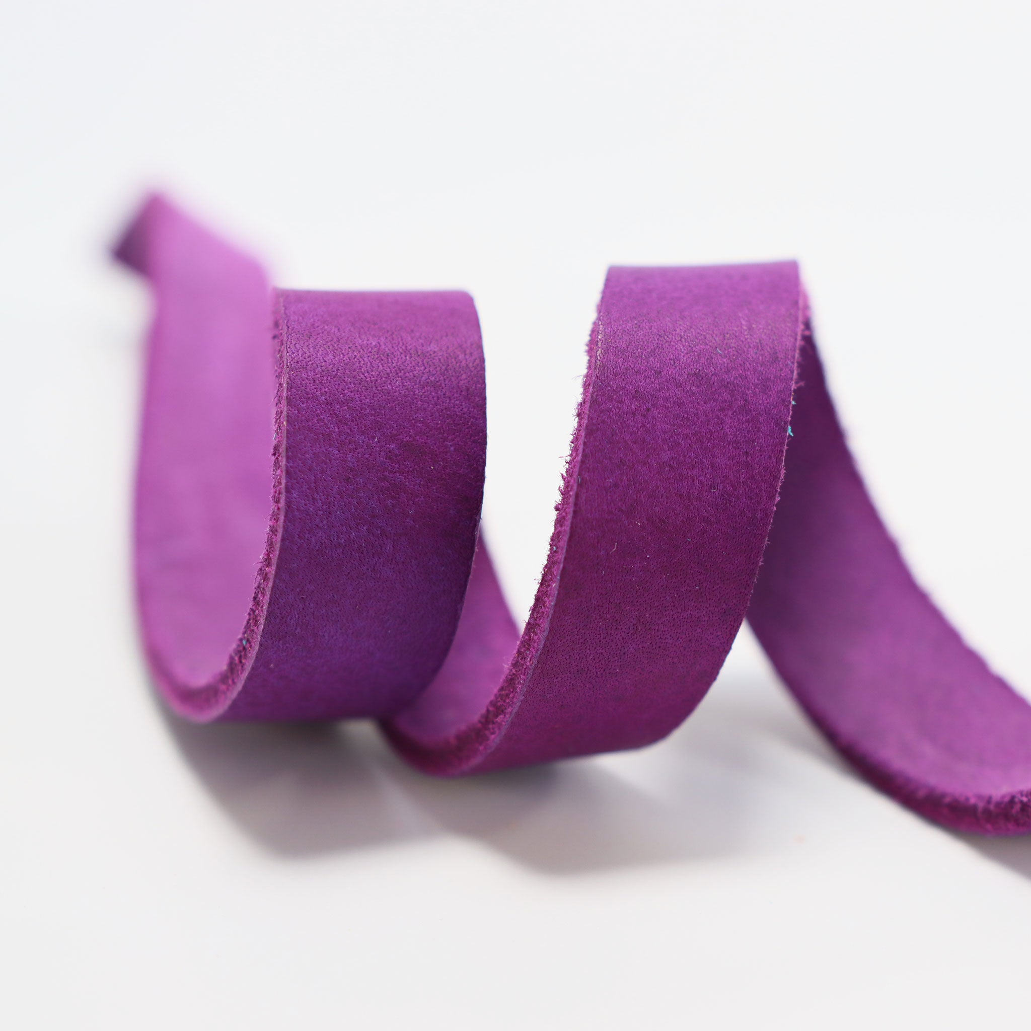 Nahaufnahme eines lilafarbenen Fettlederriemen der gerollt liegt
